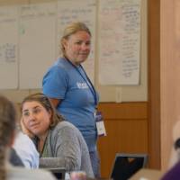 woman monitoring tables as adults discuss at a professional learning, seated indoors